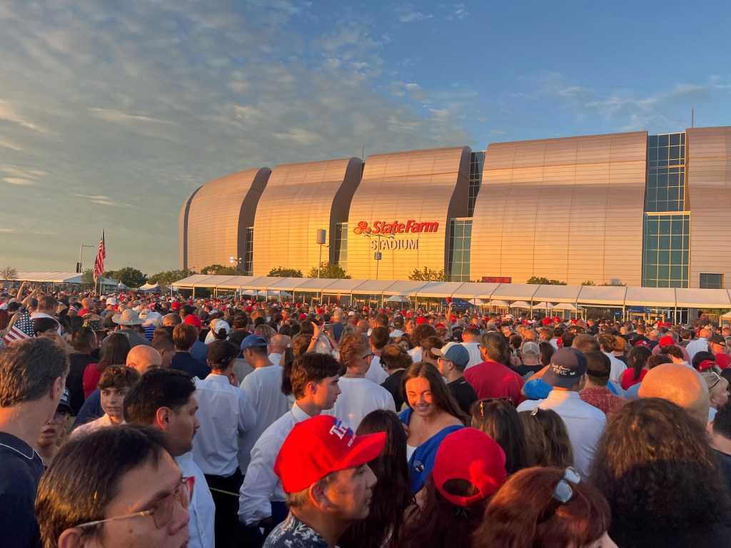 A large crowd gathered outside the State Farm Stadium during sunset, with many individuals wearing red hats and shirts.